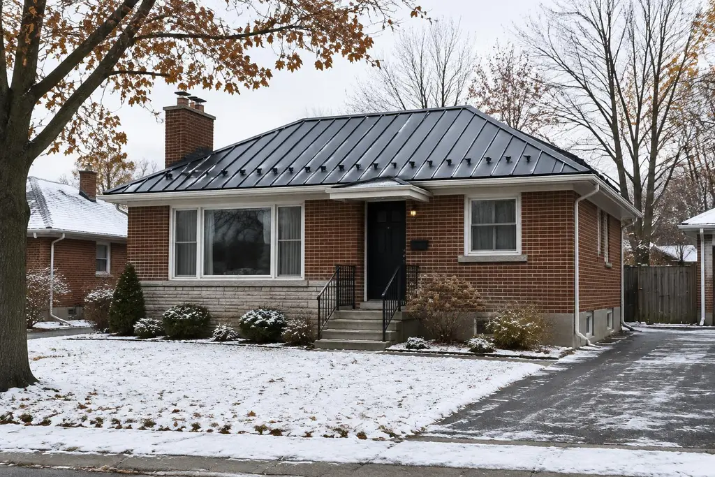 A black standing-seam metal roof with snow guards on a 1950s brick bungalow